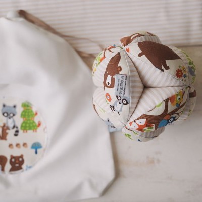 Saco de pano branco com padrão de animais da floresta e brinquedo de tecido pendurado com padrões coloridos