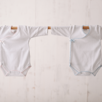 Dois bodies brancos de bebé em varão de madeira, com acabamentos cor-de-rosa e azul às bolinhas.