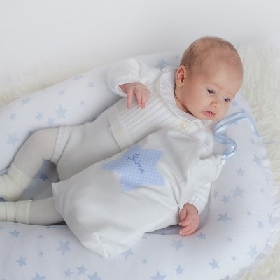 Bebé com roupa branca sobre almofadão de estrelas azul claro