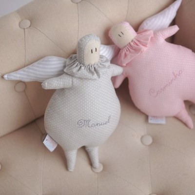 Dois bonecos de tecido em forma de anjos, cinzento e rosa, num sofá bege acolchoado