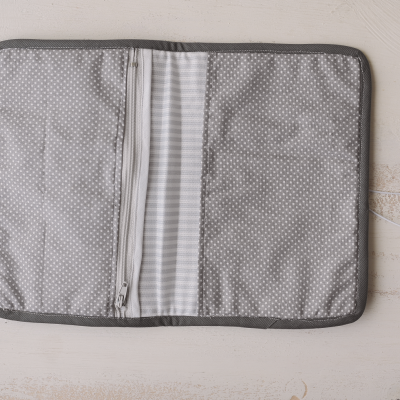 Estojo aberto cinza com padrão de pontos e riscas sobre madeira clara