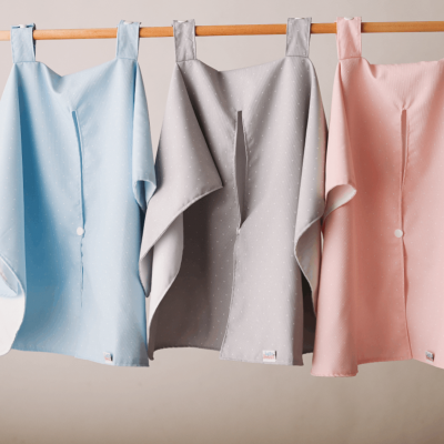 Três capas de banho azul claro, cinza e rosa penduradas em barras de madeira