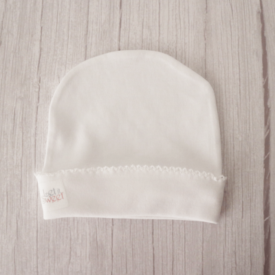Gorro branco macio com etiqueta e borda decorativa sobre madeira clara