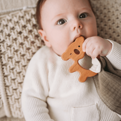 Bebé com mordedor de veado castanho e camisola branca sobre almofada trançada bege