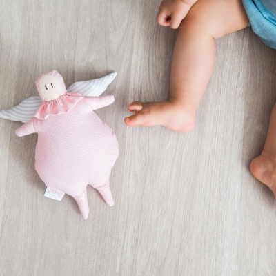 Brinquedo de pelúcia rosa com asas ao lado de bebé no chão de madeira