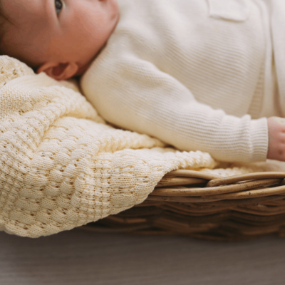 Bebé vestido com roupa de malha creme numa manta creme numa cesta de vime.