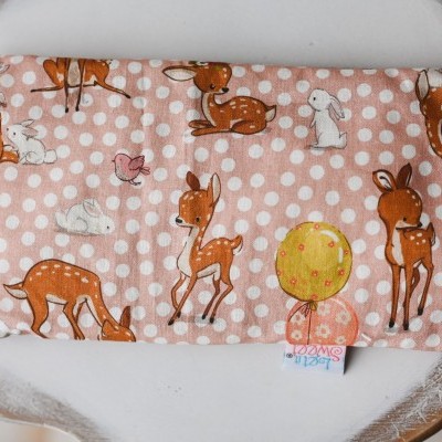 Almofada térmica cor-de-rosa com bolinhas brancas e desenhos de cervos e coelhos.