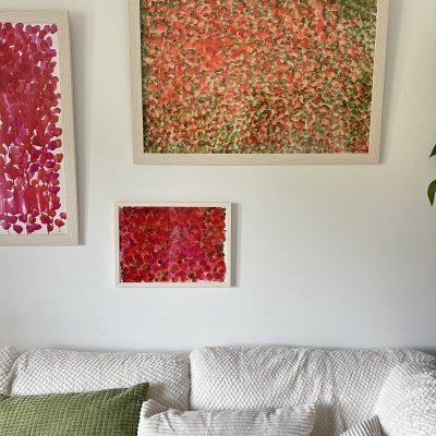 Três quadros florais em molduras brancas sobre sofá branco com almofadas verde e branca.