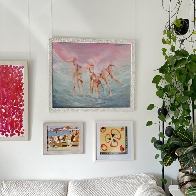 Parede com quatro quadros coloridos, sofá branco e plantas em vasos na sala