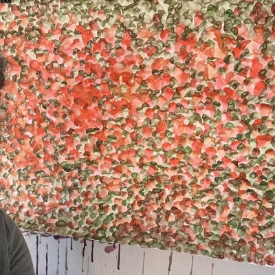 Tecido decorativo artesanal colorido pendurado na parede com parte do rosto de uma pessoa com óculos visível