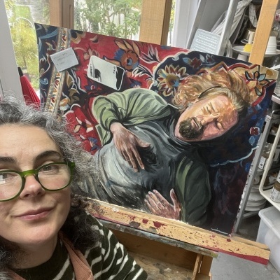 Pintura a óleo de homem deitado num tapete vermelho com padrões florais em cavalete, mulher com óculos verdes à frente