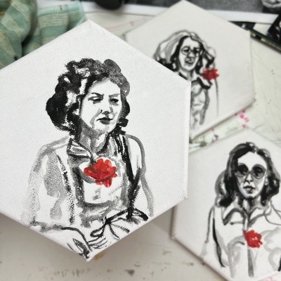 Três telas hexagonais com desenhos de mulheres em tinta preta e detalhe em vermelho em mesa branca