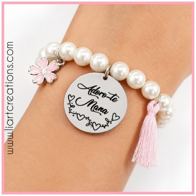 Pulseira de contas tipo pérola branca com pendente metálico redondo gravado e pendentes decorativos rosa em pulso.