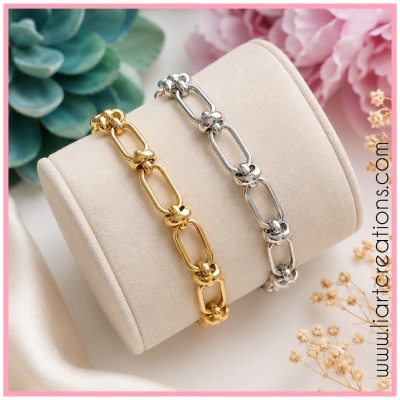 Duas pulseiras metal dourado e prateado em suporte almofadado com flores ao fundo