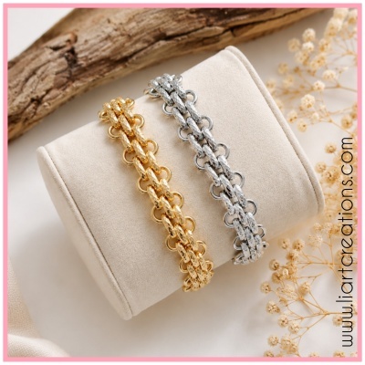 Braceletes dourado e prateado entrelaçados sobre almofada bege com decoração natural