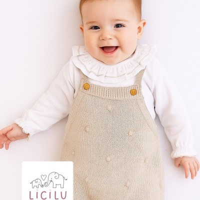 Bebé com camisola branca de gola com folhos e jardineira bege de malha