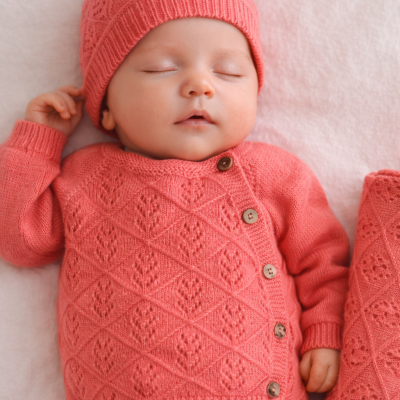 Bebé dormindo com roupa de malha cor-de-rosa com botões e padrão entrelaçado