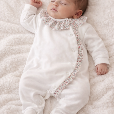 Bebé vestido com macacão branco com detalhes florais a dormir numa manta branca