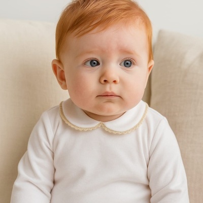 Bebé ruivo com body branco sentado no sofá bege