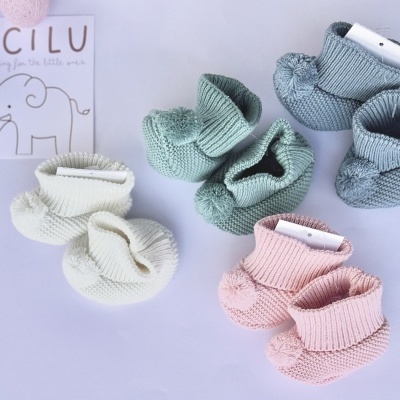 Três pares de sapatinhos de bebé em malha azul, creme e rosa com textura canelada e pompons