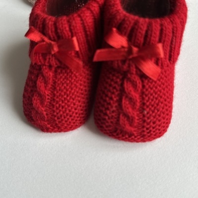 Sapatinhos de bebé vermelhos em tricot com laços e padrão de trança central.