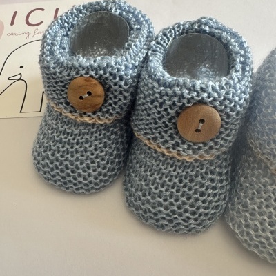 Botas de bebé de malha azul com botão de madeira em fundo branco