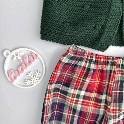 Roupa com malha verde e calça xadrez vermelha com objeto branco e rosa escrito Lucilu.