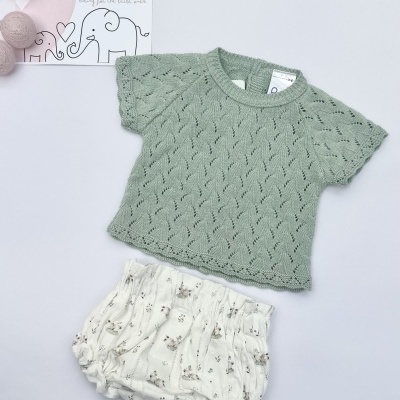 Conjunto de bebé com t-shirt verde e calções brancos com padrão floral e cartão LICILU ao lado.