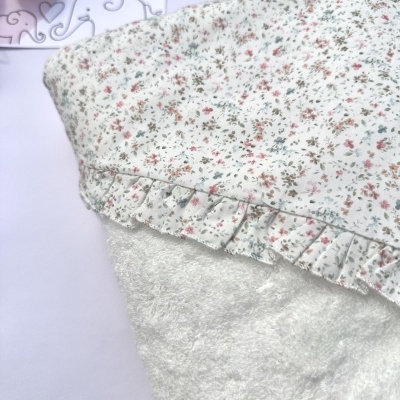 Capa de bebé branca com padrão floral e folho, placa LICILU ao fundo