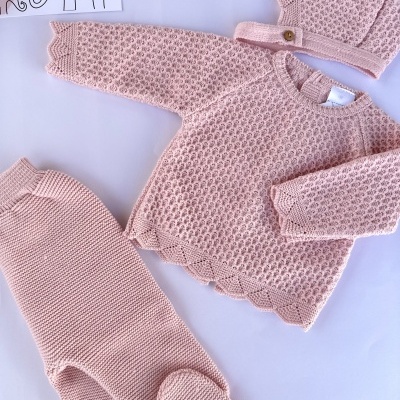 Conjunto de bebé cor-de-rosa em malha com suéter, calças e gorro sobre fundo branco com ilustração de elefantes.