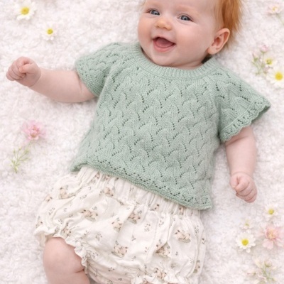 Bebé deitado com camisola verde clara de malha e calções brancos com padrão floral