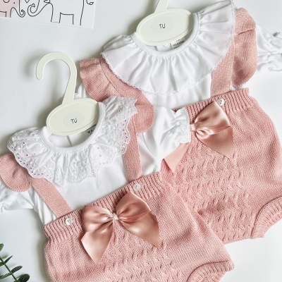 Dois conjuntos de roupa para bebé rosa e branco com laços e golas bordadas, pendurados em cabides sobre fundo branco.
