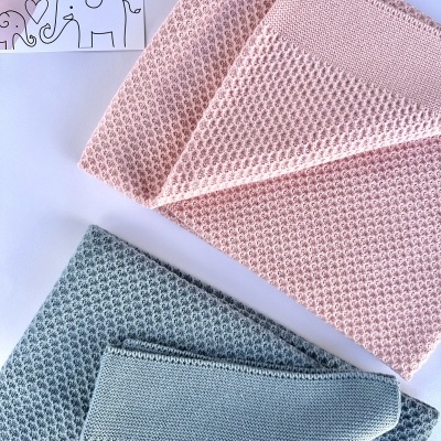 Duas mantas de bebé em malha com padrão, rosa e cinza, sobre fundo branco com etiqueta decorativa.