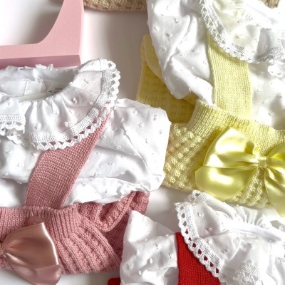 Três conjuntos de roupa de bebé com camisa branca e jardineiras coloridas com laços de cetim