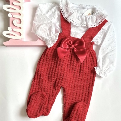 Conjunto de bebé com body branco de gola rendada e jardineiras vermelhas com laço.