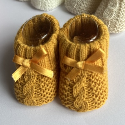 Sapatinhos de bebé amarelo-mostarda tricotados com laço de fita e outros sapatinhos creme ao fundo