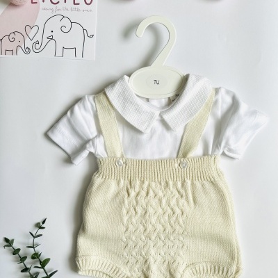 Roupa de bebé branca e creme num cabide branco com decoração rosa e verde