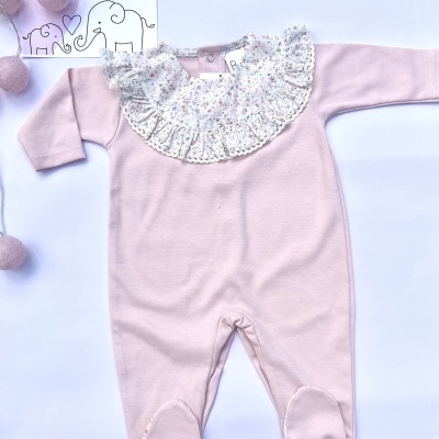 Macacão rosa claro para bebé com gola floral e pés fechados sobre fundo branco com cartão de marca e luzes cor de rosa.