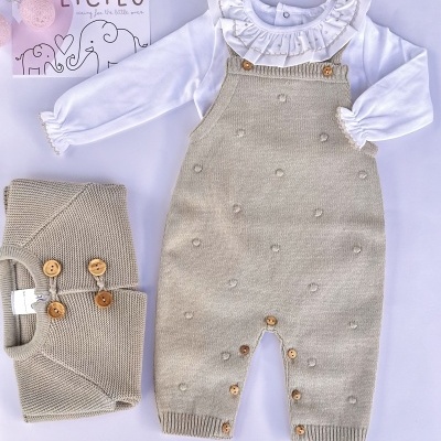 Conjunto de roupa de bebé com camisola branca e macacão beige de malha com botões de madeira, e casaco bege de malha dobrado ao lado.
