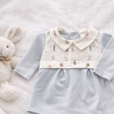 Vestido de bebé azul claro com gola branca e decoração náutica, ao lado de coelho de pelúcia branco