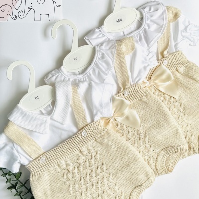 Roupas de bebé branca e bege com malha e laço em cabides