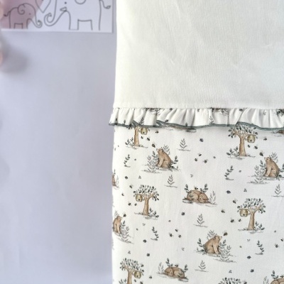 Roupa infantil branca com padrão de coelhos e árvores e folho, etiqueta LICILU ao fundo