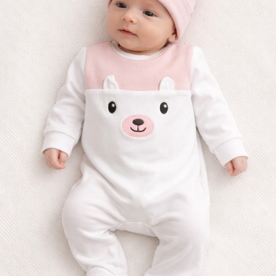 Bebé com macacão branco e rosa com rosto de urso bordado e gorro rosa com orelhas