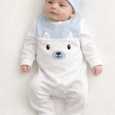 Bebé a usar pijama branco e azul claro com rosto de urso bordado e gorro azul com orelhas