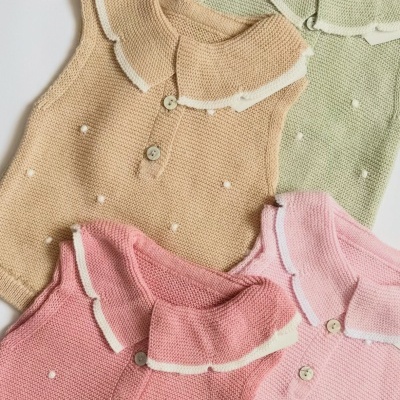 Camisolas de bebé em malha com gola de babado e botões em várias cores pastel sobre fundo branco.