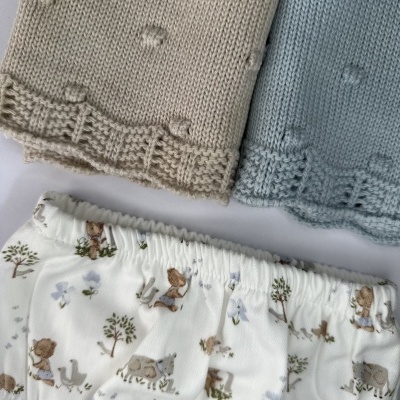 Roupas de bebé: calças de malha bege e azul claro com pontos e calção branco estampado com animais e árvores.