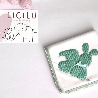 Fralda branca com borda verde e decoração de coelhos de croché, cartão LICILU com elefantes rosa ao lado