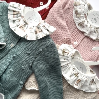 Casacos de malha para bebé com golas estampadas em cabides brancos sobre fundo branco