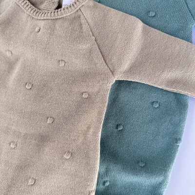 Conjuntos de roupa de bebé em malha bege e verde-azulado com pequenos bordados em círculo.