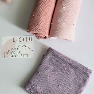 Três mantas de malha fina em tons rosa com pompons, ao lado de cartão LICILU e elefantes